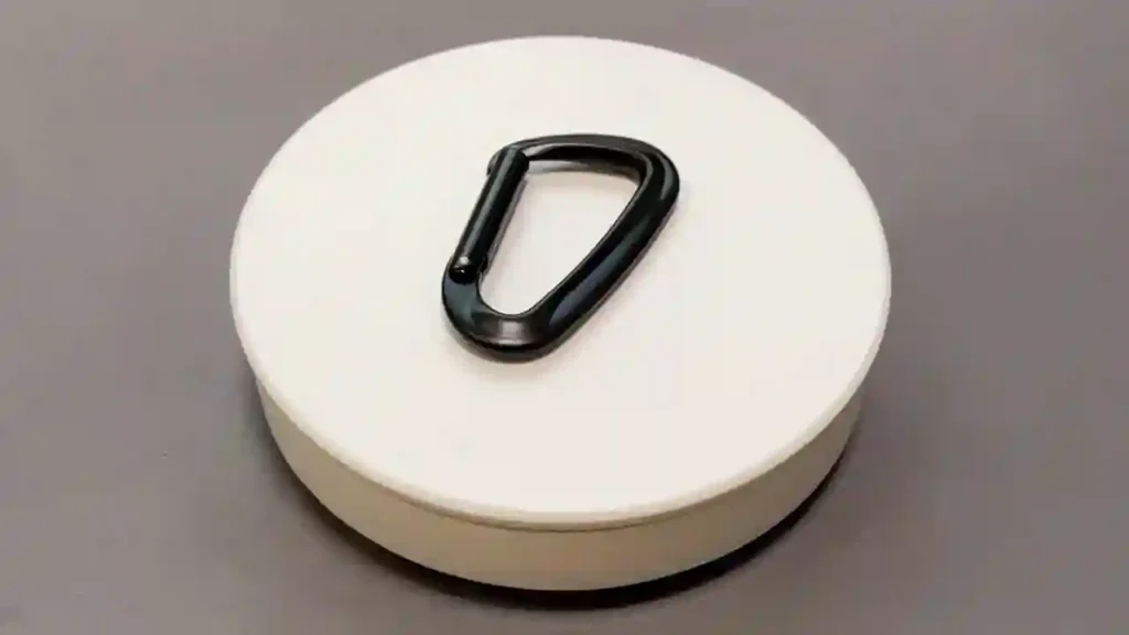 A sleek, black D701S1 model aluminum carabiner featuring a smooth gate mechanism, centered on a white pedestal with a neutral gray background. The lighting highlights the metallic texture and D-ring shape of the hardware.